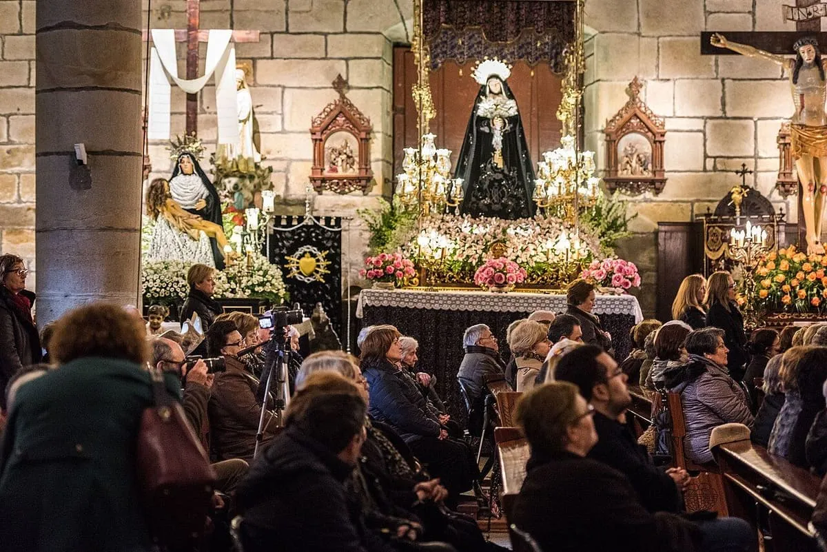Una multitud llena la iglesia durante una ceremonia de Semana Santa, con la imagen de la Virgen vestida de negro al fondo