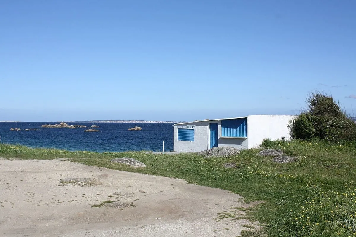 Caseta azul y blanca junto a la playa de O Carreiro, con el mar y unas islas al fondo
