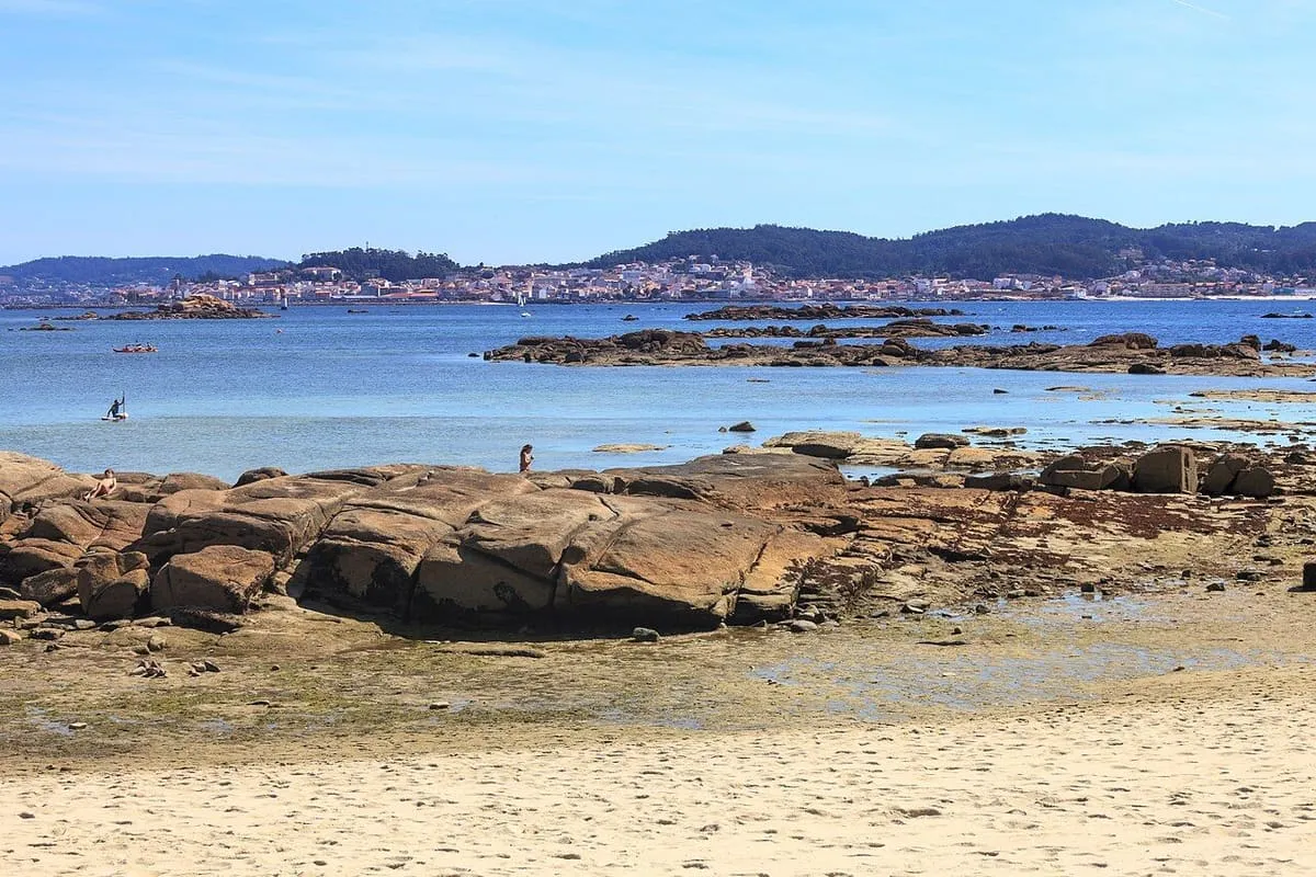 Rocas y arena de la costa del parque natural de Carreirón, con la ría al fondo
