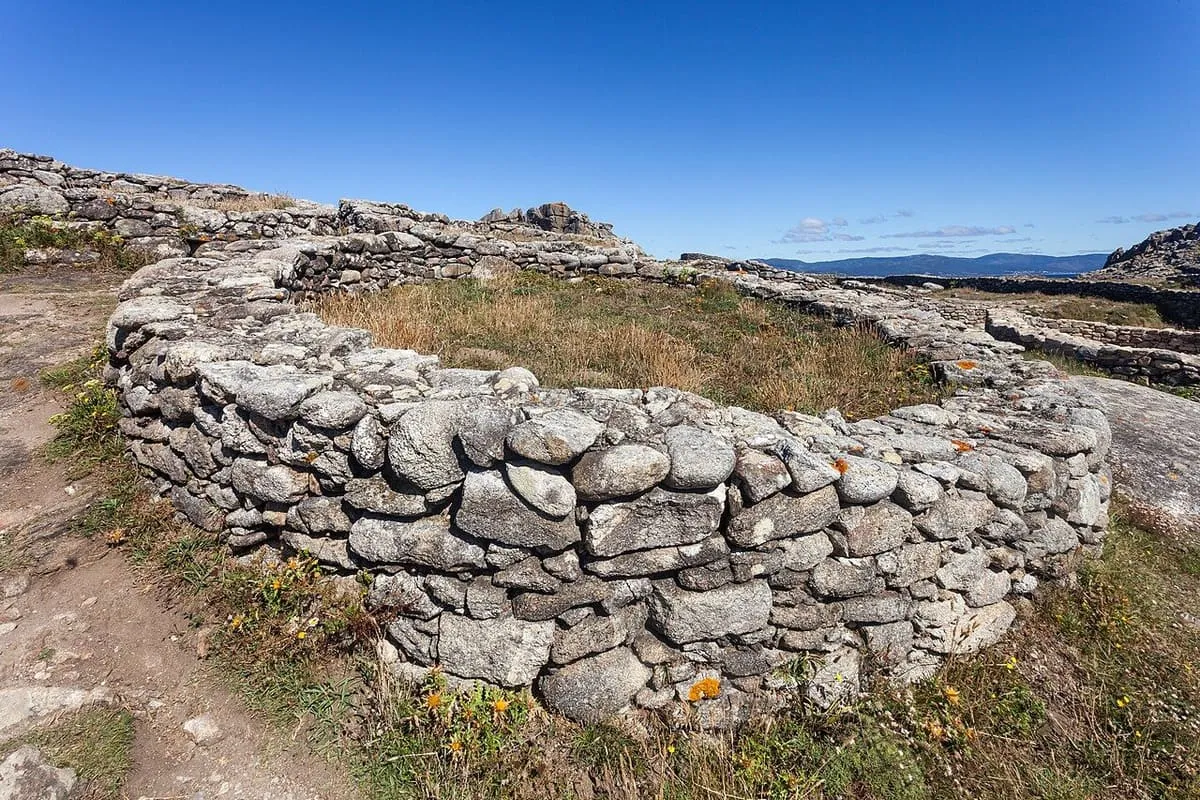 Muro circular de piedra de una vivienda del castro, con el Atlántico al fondo