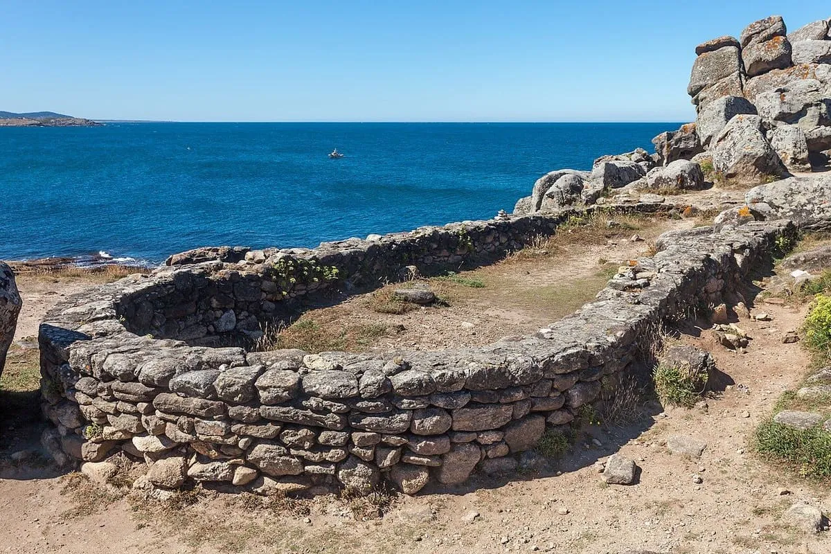 Base oval de piedra de una vivienda del castro, con el mar al fondo