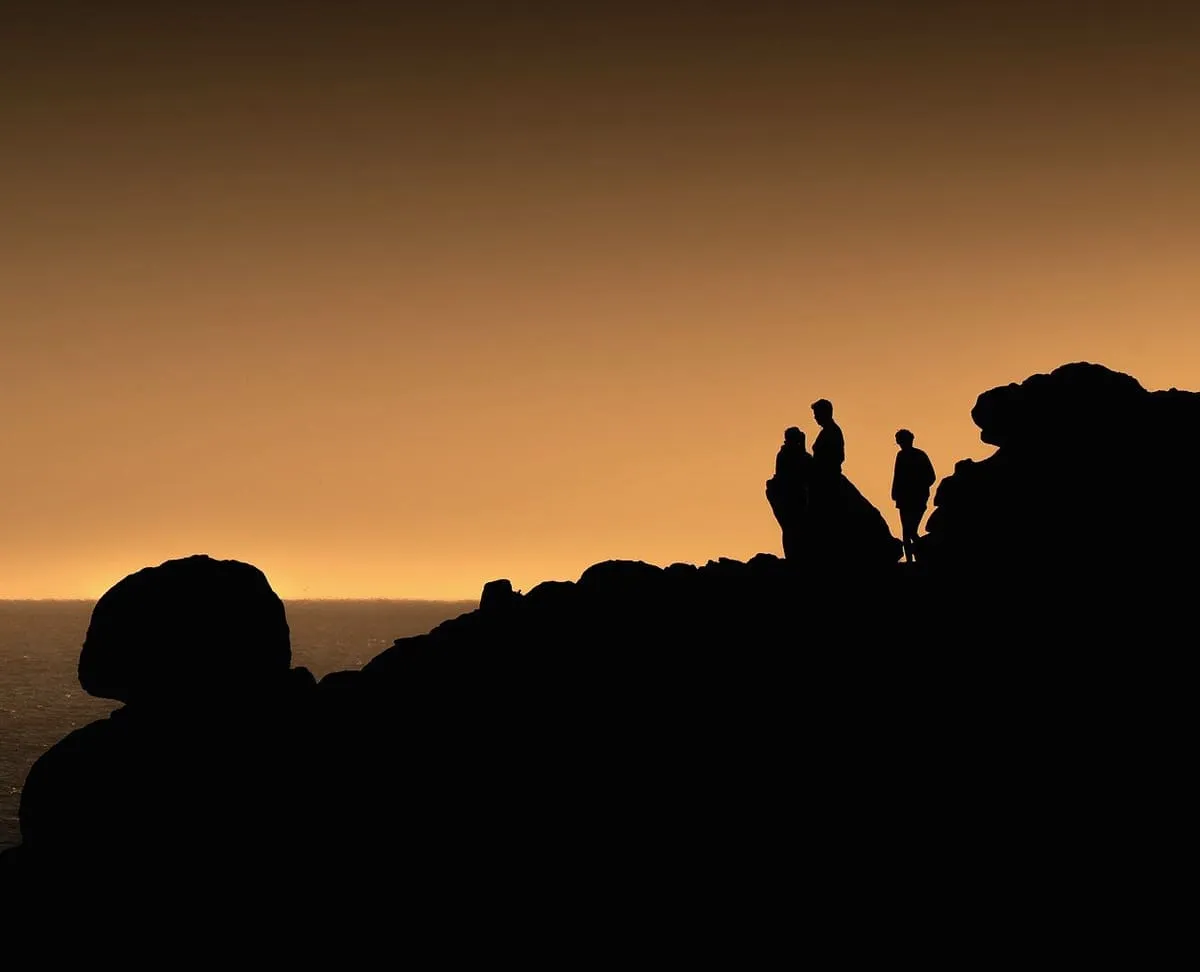 Siluetas de varias personas sobre las rocas del castro, con el cielo naranja del atardecer
