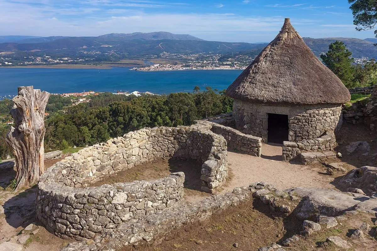 Vivienda circular con techo de paja reconstruida en el castro de Santa Trega, con el mar al fondo