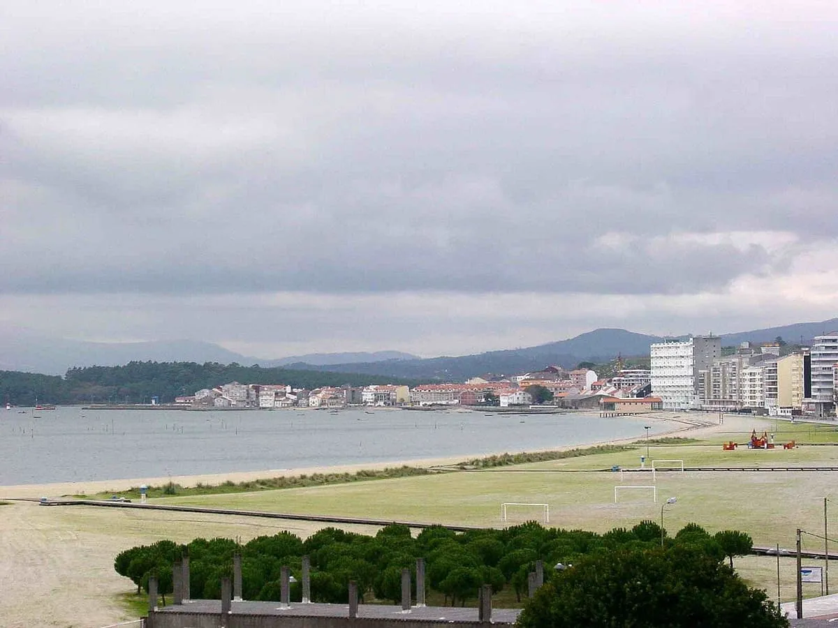 Vista de la playa y del paseo de Vilagarcía de Arousa con un campo verde en primer plano