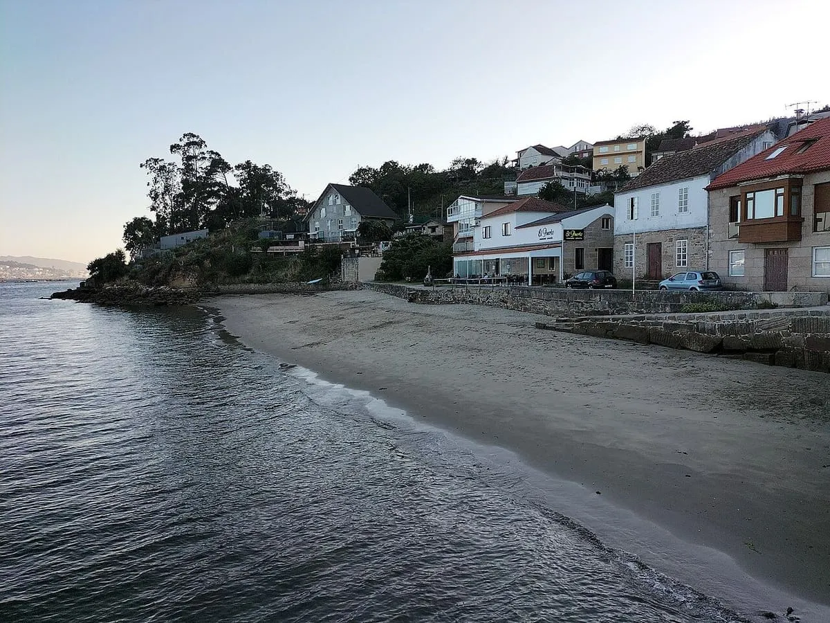 Pequeña playa de arena junto a las casas de Domaio al atardecer