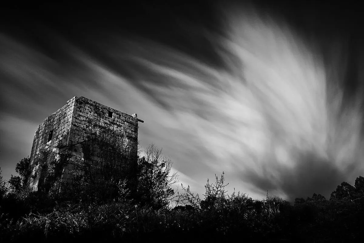 La torre de Guimarei recortada sobre un cielo con nubes en blanco y negro