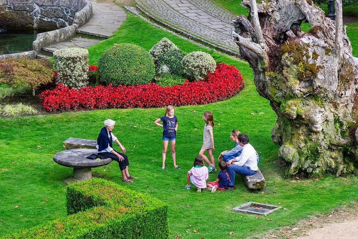 Familia sentada en el césped del jardín del castillo de Soutomaior, junto a un parterre de flores rojas y un tronco centenario