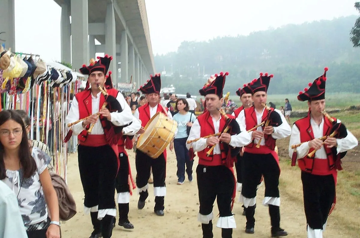 Un grupo de gaiteros con traje tradicional rojo y negro desfilando durante la Romería Vikinga