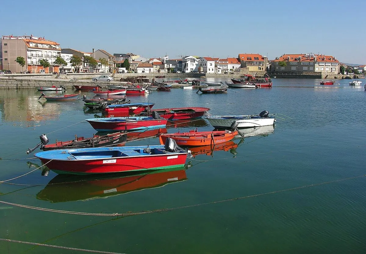 Barcas rojas y blancas amarradas en el agua verdosa del puerto de A Illa de Arousa, con casas al fondo