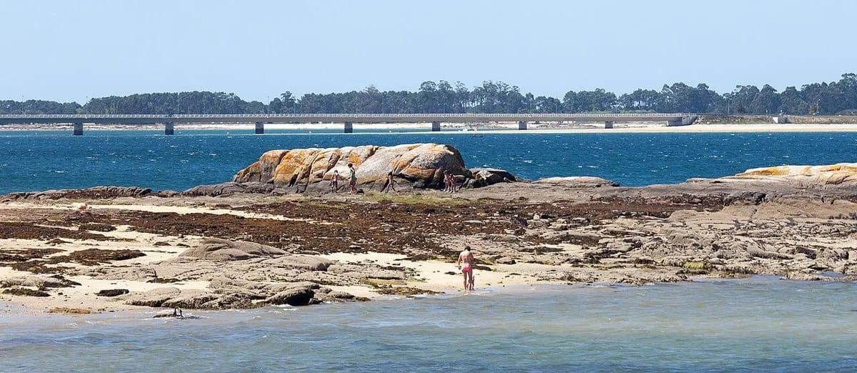 Playa de rocas con el puente de la isla al fondo