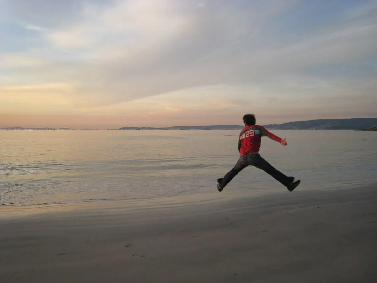 Una persona saltando en la arena de Lapamán con el cielo del atardecer