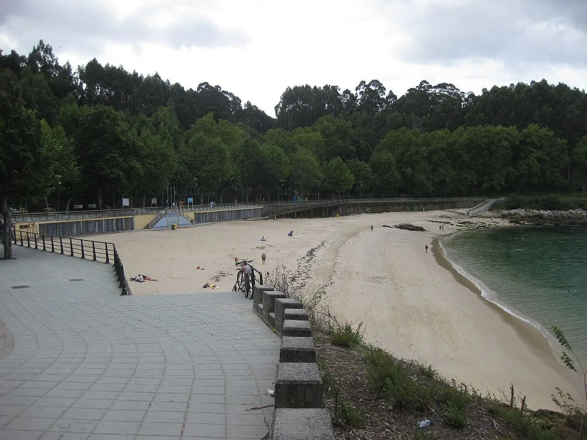 Paseo de baldosas junto a la playa de Portocelo, con la arena y el bosque de pinos