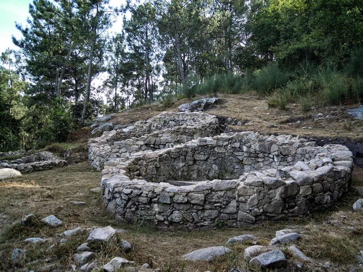 Casas circulares restauradas del castro da Subidá, con bosque al fondo