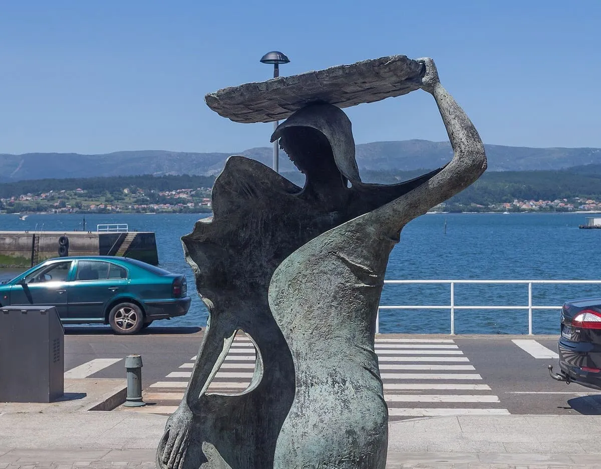 Escultura de una mariscadora con una bandeja de piedra sobre la cabeza, frente a la ría de Arousa