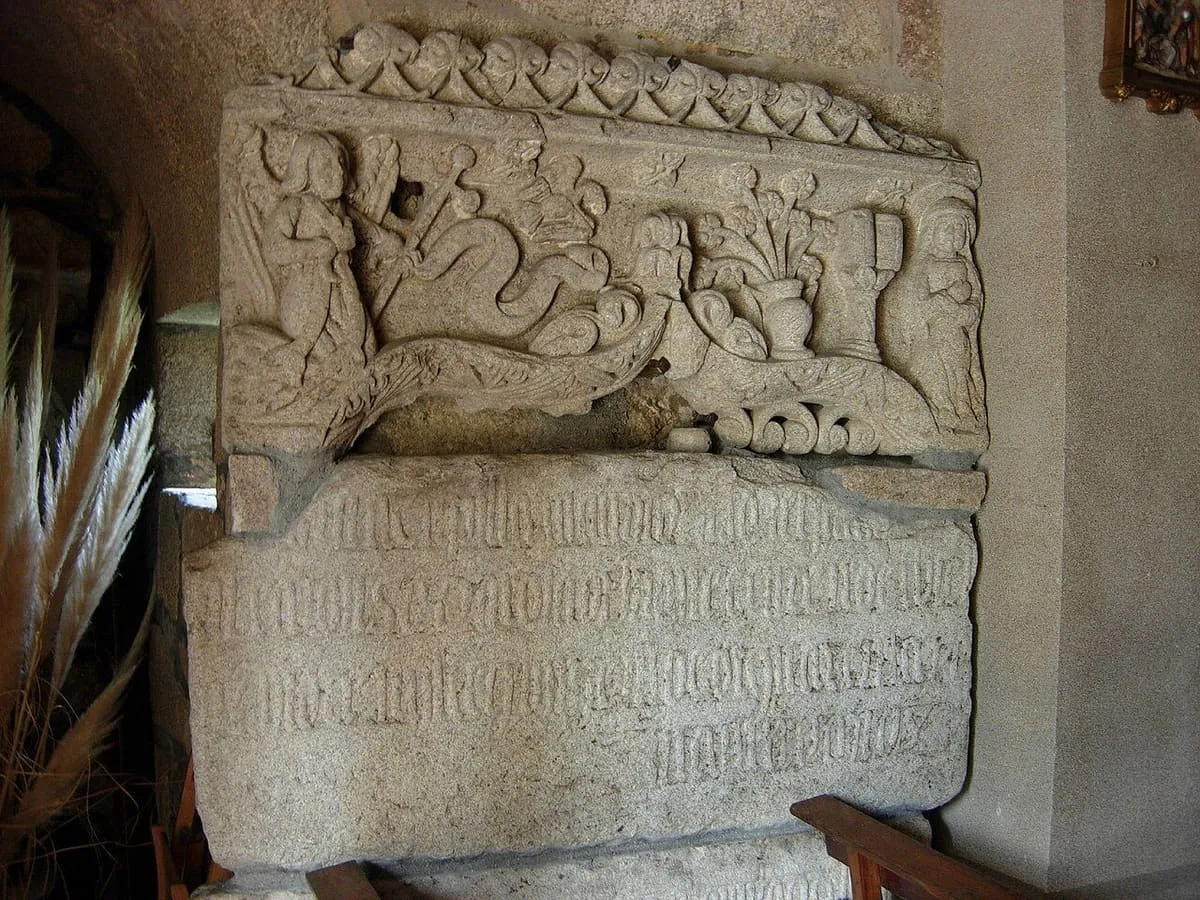Dos figuras en una hornacina sobre un epígrafe en el muro de San Martiño de Meis