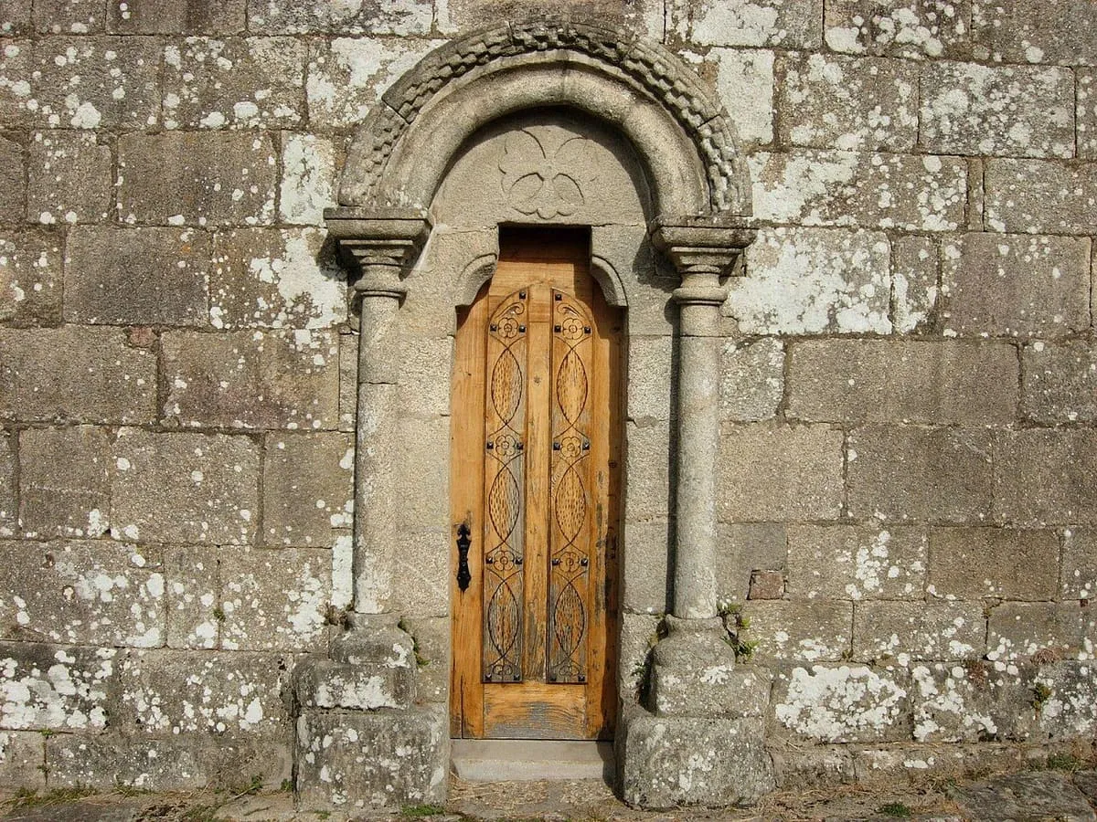 Portada de arco de medio punto con jambas y una puerta de madera labrada en San Martiño de Meis