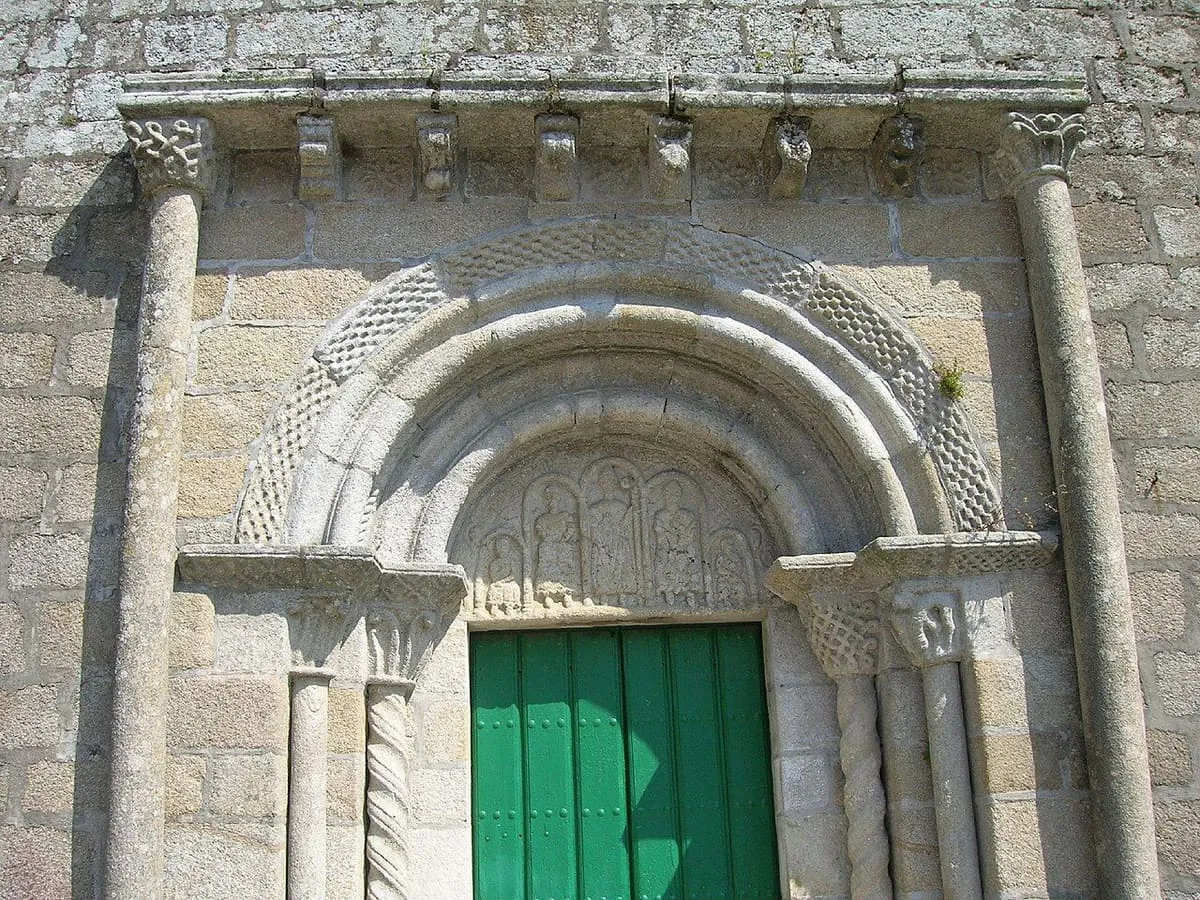 Portada románica de San Martiño con arquivoltas, columnas y un tímpano esculpido, bajo una puerta verde