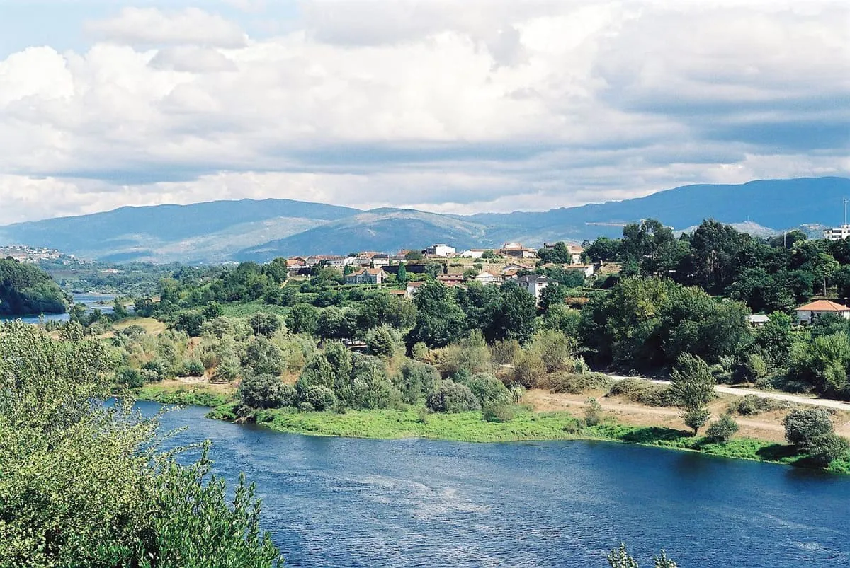 El Miño entre orillas verdes, con las casas de Monção y montañas al fondo, visto desde Galicia