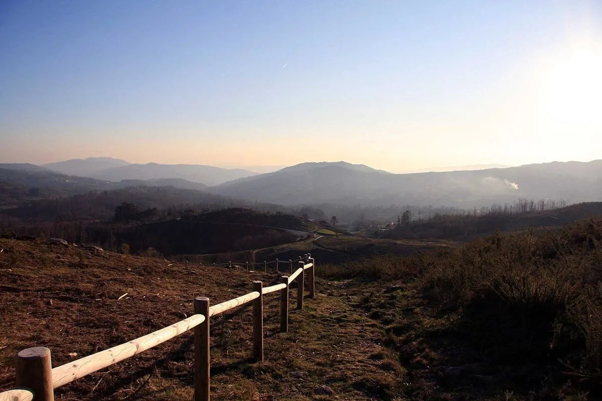Vista del monte de Tourón al atardecer, con una valla de madera y montañas al fondo