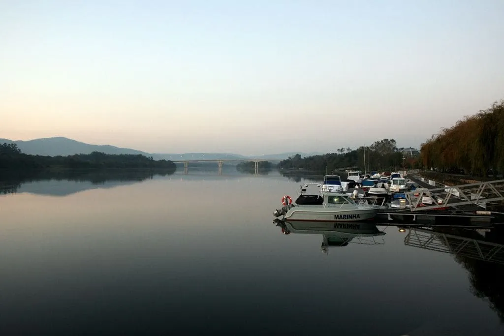 Embarcaciones amarradas en un muelle del Miño al amanecer, con un puente al fondo