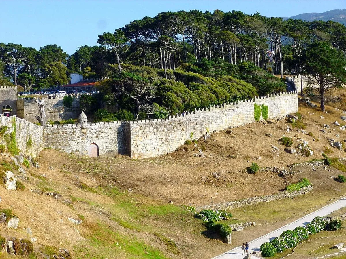 Muralla de Monterreal recorriendo una ladera de hierba bajo el pinar de Monte Boi