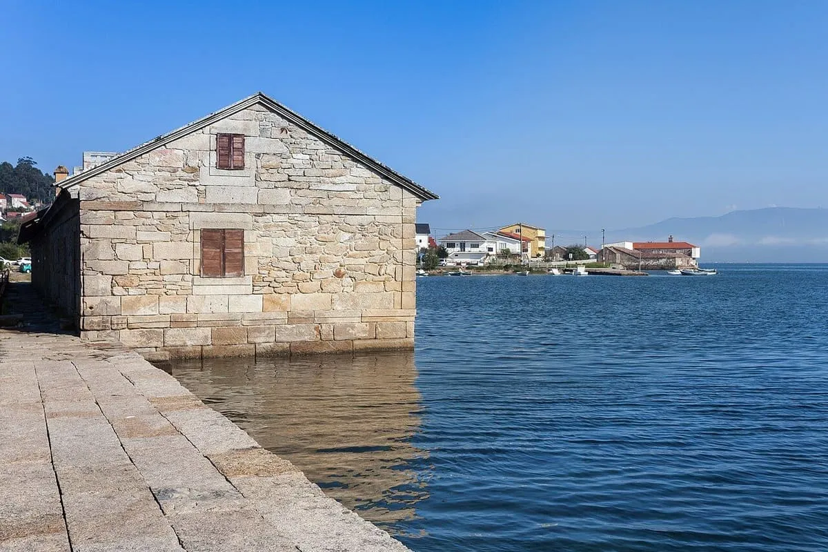 Edificio de piedra del molino sobre el agua, con la ría de Muros e Noia al fondo