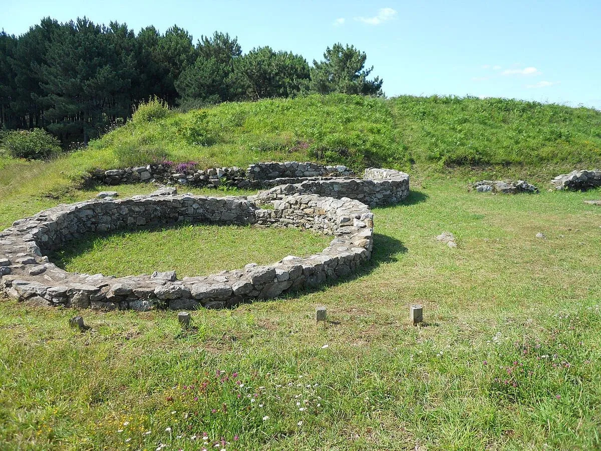 Base circular de una vivienda de Neixón, con una loma cubierta de hierba detrás