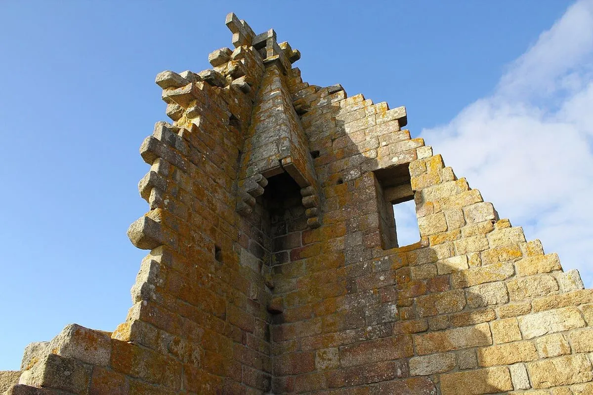 Remate escalonado de la torre de San Sadurniño, con ménsulas de piedra y una ventana, visto desde abajo