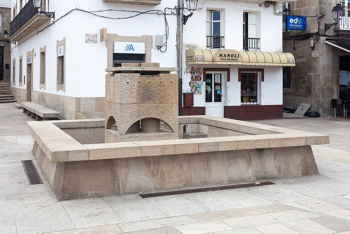 Fuente de piedra en una plaza de Muros, con casas blancas al fondo