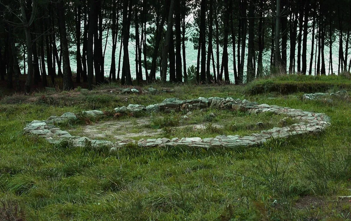Vivienda circular de piedra entre pinos, con la ría de Arousa detrás