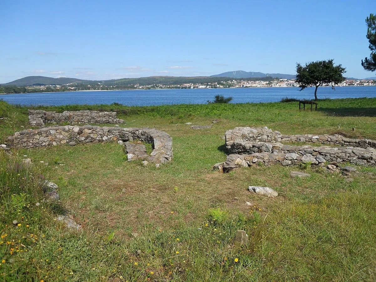 Muros de piedra de los castros de Neixón sobre la hierba, con la ría y la costa de enfrente