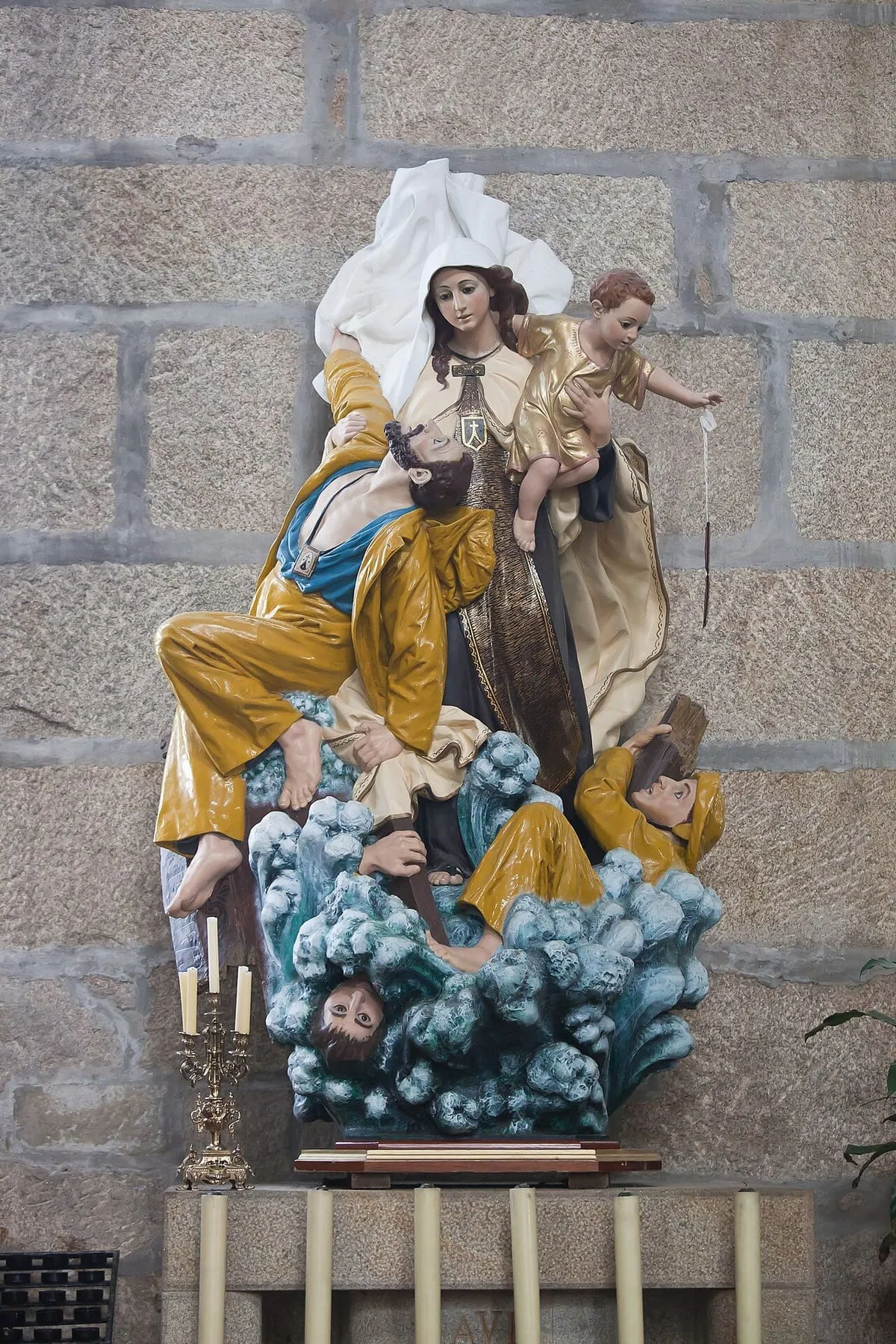 Grupo escultórico policromado de figuras en una barca sobre olas, ante un muro de granito del templo
