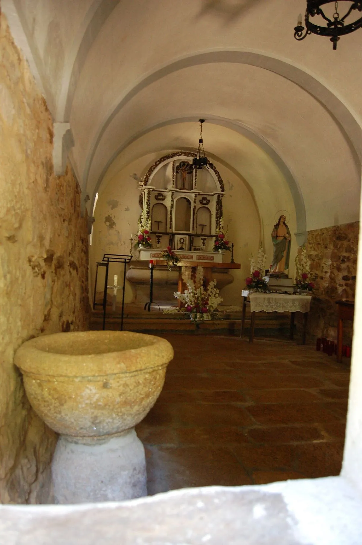 Interior de la ermida con un retablo pequeño, una imagen de la santa y una pila de piedra