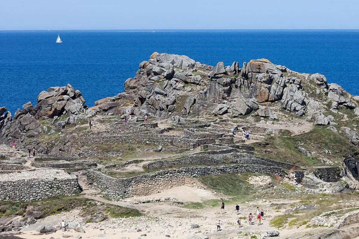 Visitantes caminan entre las rocas de la parte alta del castro, con el mar al fondo