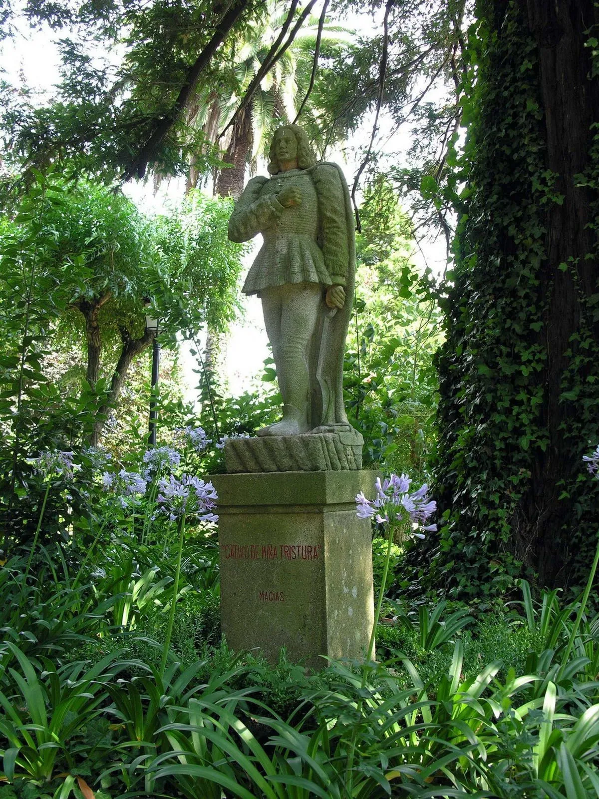 Estatua de Macías o Namorado entre jazmines y arbustos del jardín
