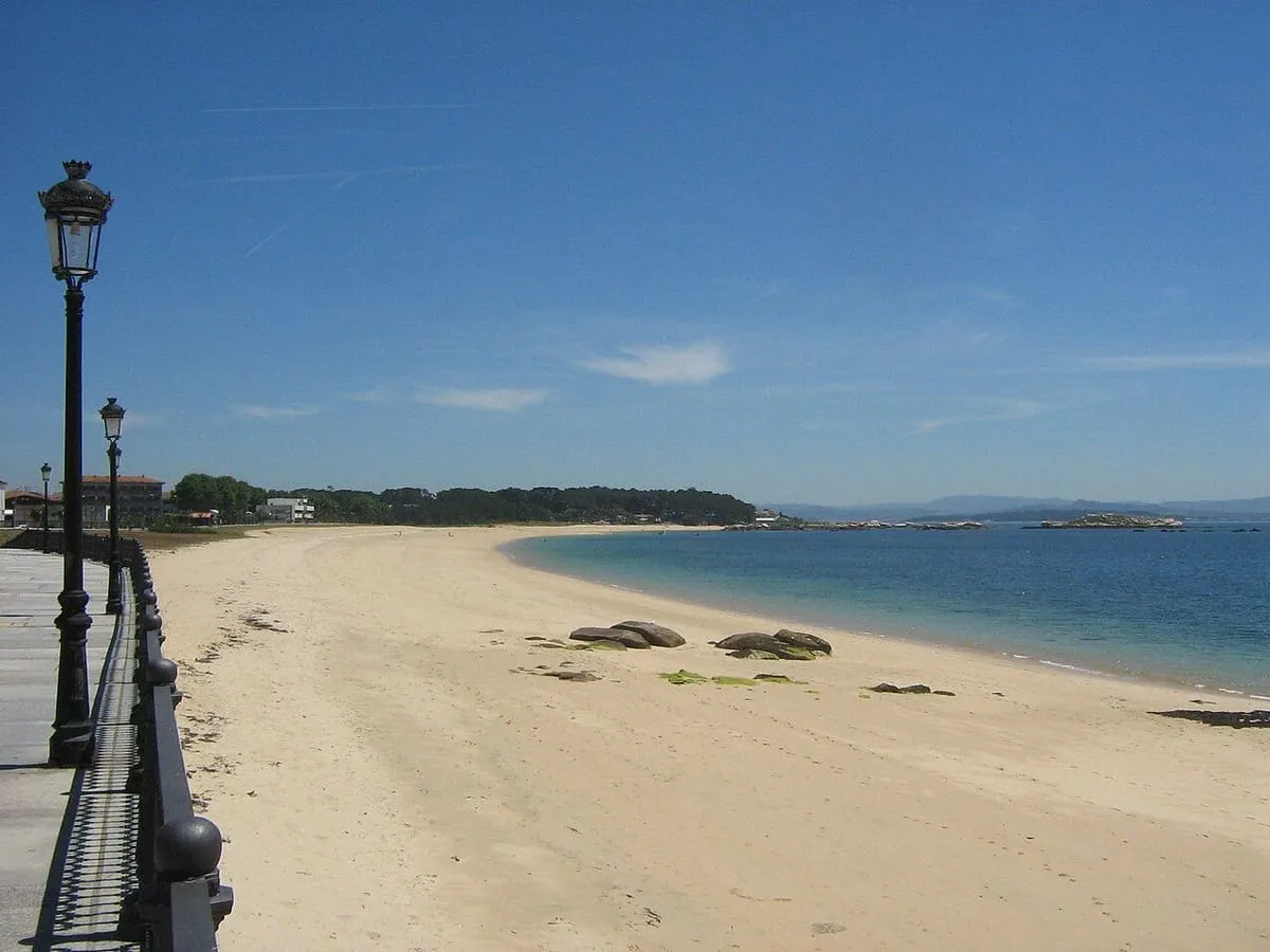 Paseo con farolas junto al arenal de Coroso, con la arena vacía y el mar en calma