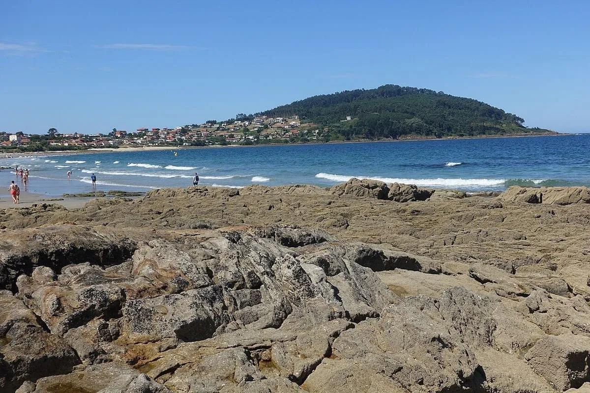 Rocas y olas en la orilla de la playa de Patos, con el monte al fondo
