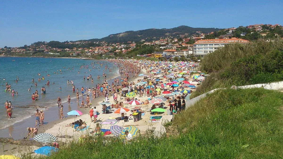 Playa de Patos llena de sombrillas en verano, con el monte Lourido al fondo