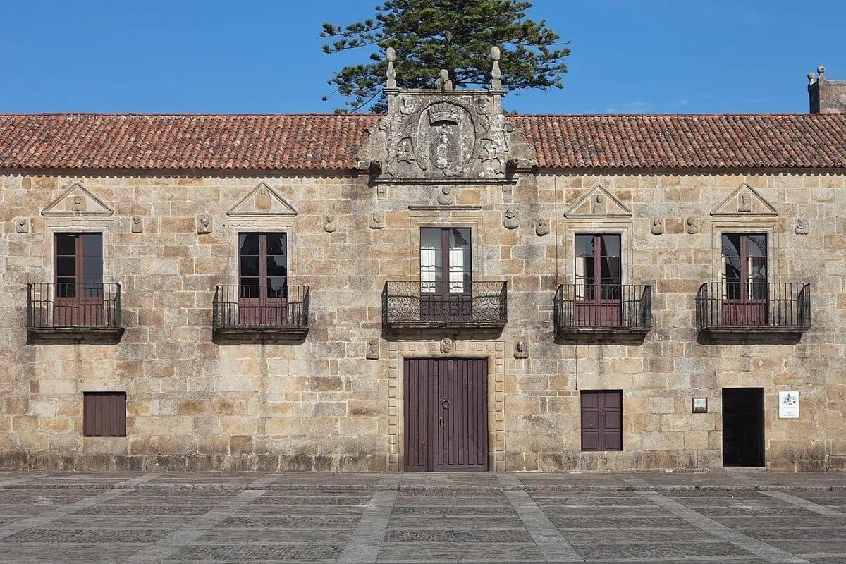 Fachada del Pazo de Fefiñáns, de piedra, con escudo sobre la puerta y balcones, frente a su plaza