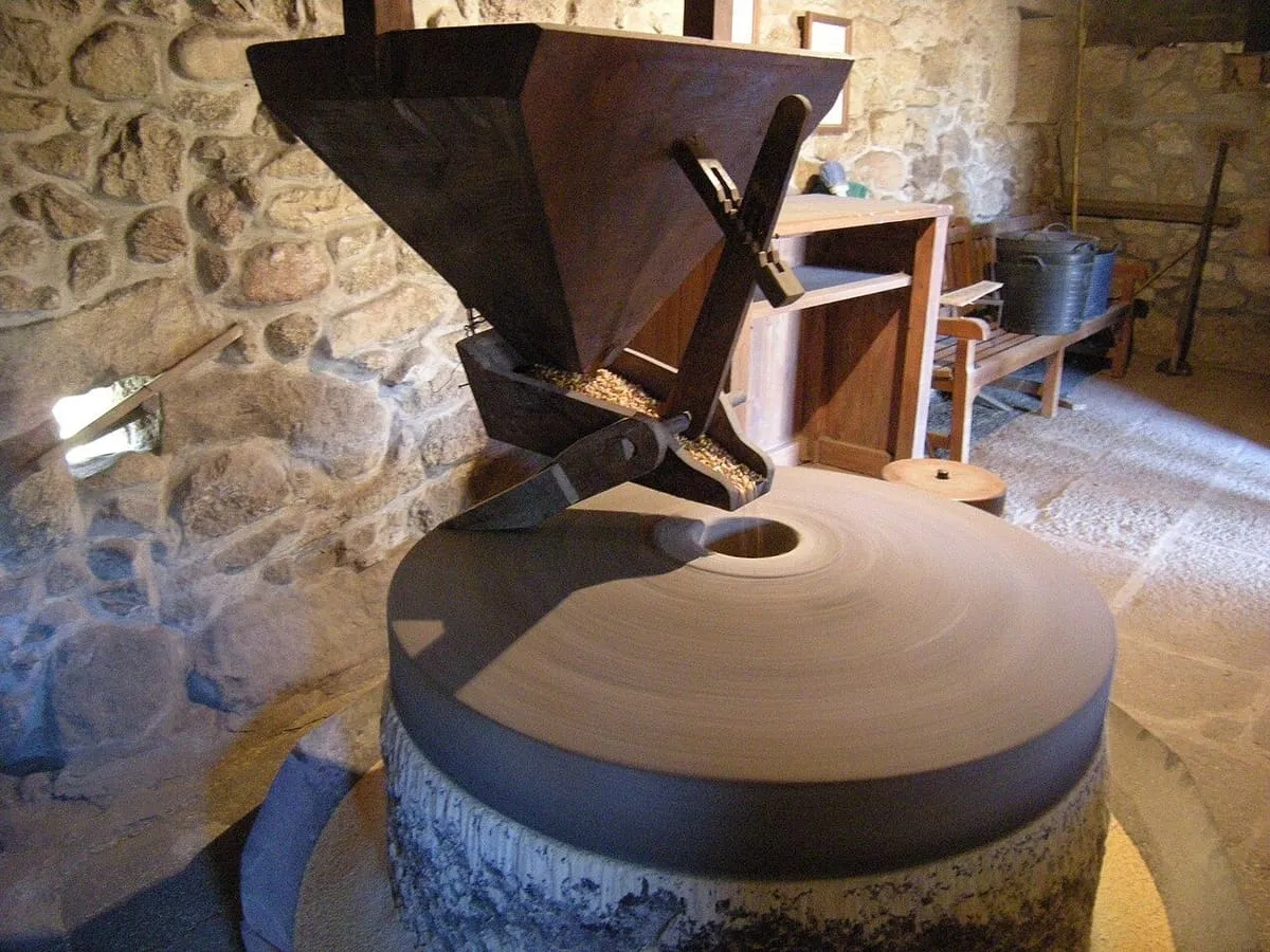Interior de un molino restaurado con la piedra de moler y la tolva de madera