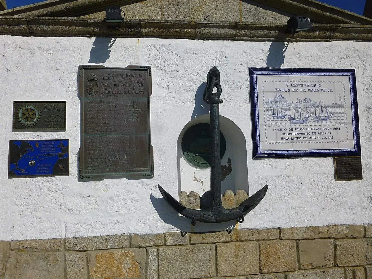Placas conmemorativas y un ancla en un muro blanco, recuerdo de la arribada de la Pinta en 1493