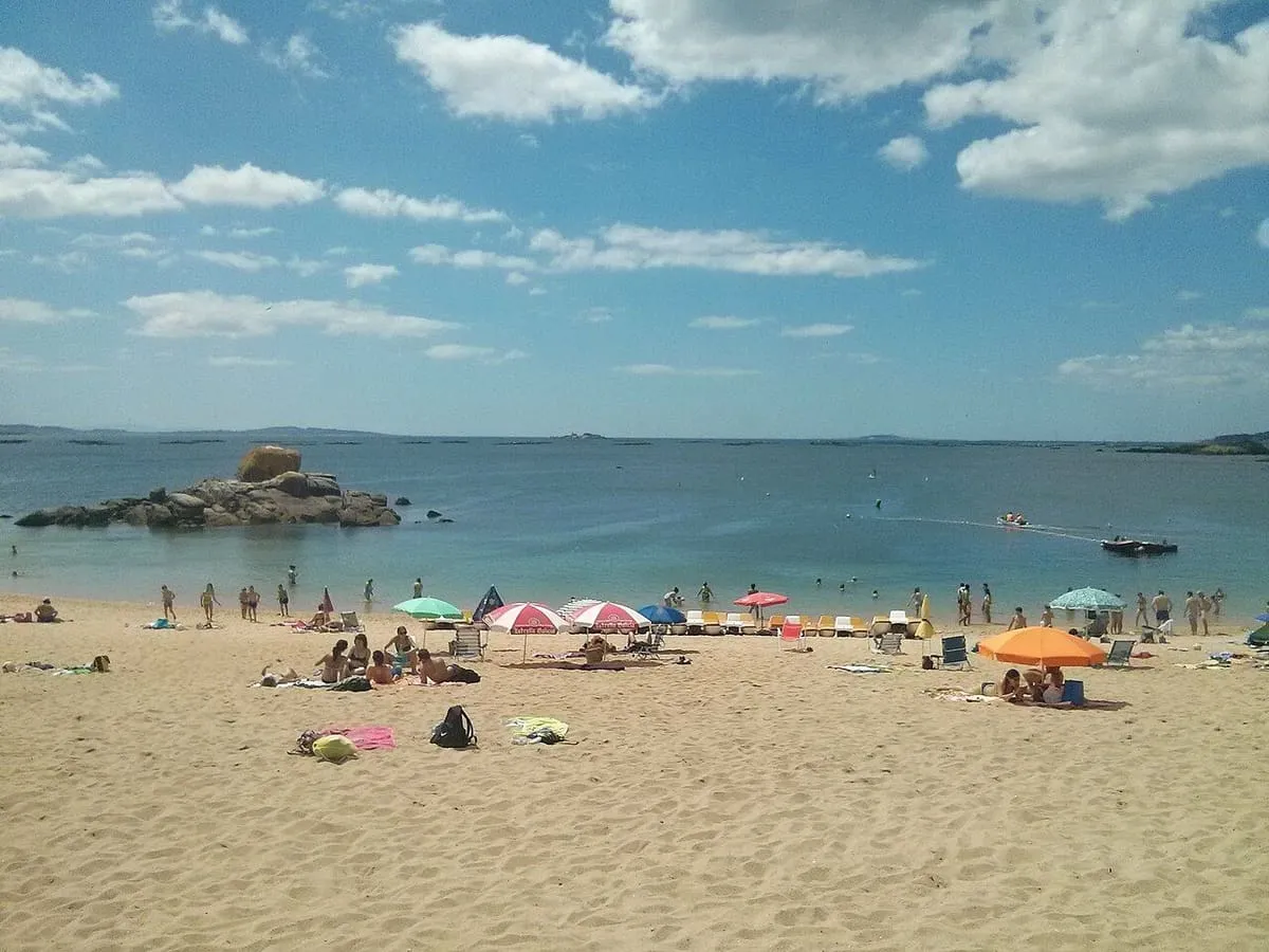 Bañistas en la playa de Lombiña-Cabío, con rocas y la ría detrás
