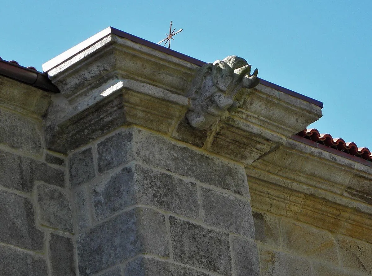 Figura de piedra sobre el tejado de la fachada de la iglesia, junto a una cornisa labrada