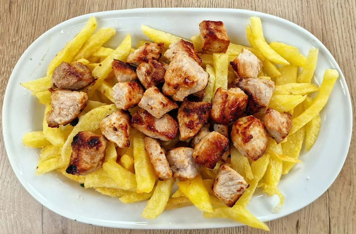 Un plato de raxo, tacos de lomo de cerdo, con patatas fritas, servido en un restaurante de Combarro