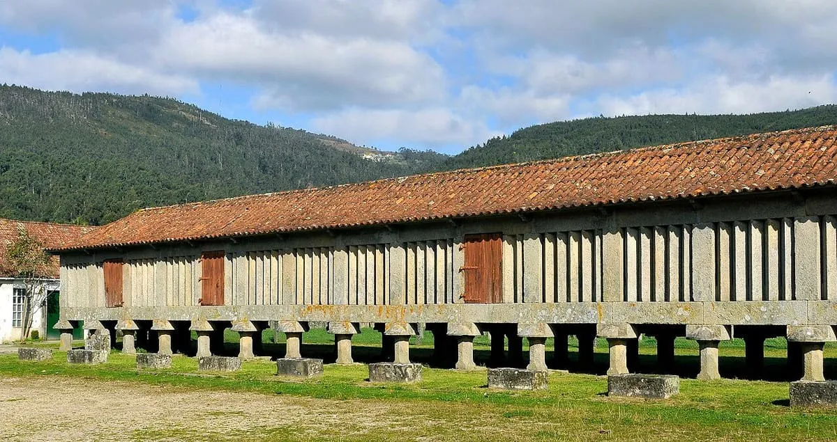 Hórreo larguísimo de piedra y madera sobre decenas de pies, con montes al fondo