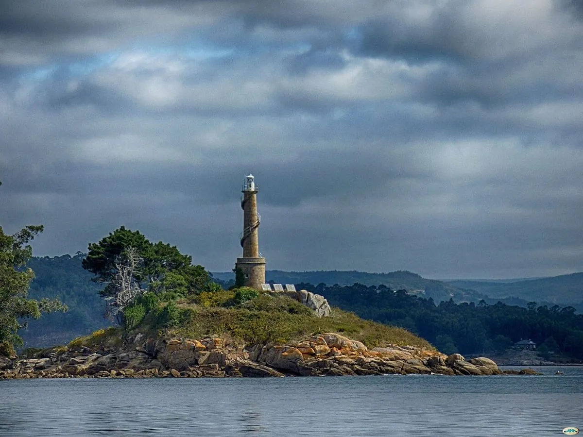El faro de la isla de Tambo sobre una lengua de hierba y rocas, con el cielo cubierto