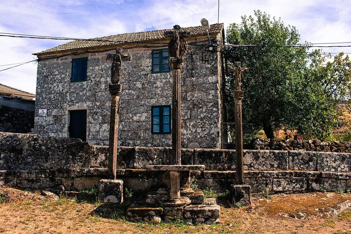 Calvario de piedra de A Insua con cruceiros rematados en cruces, junto a una casa de piedra