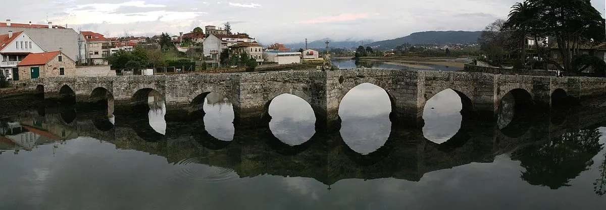 Puente medieval de arcos de piedra reflejados en el río Miñor, en A Ramallosa