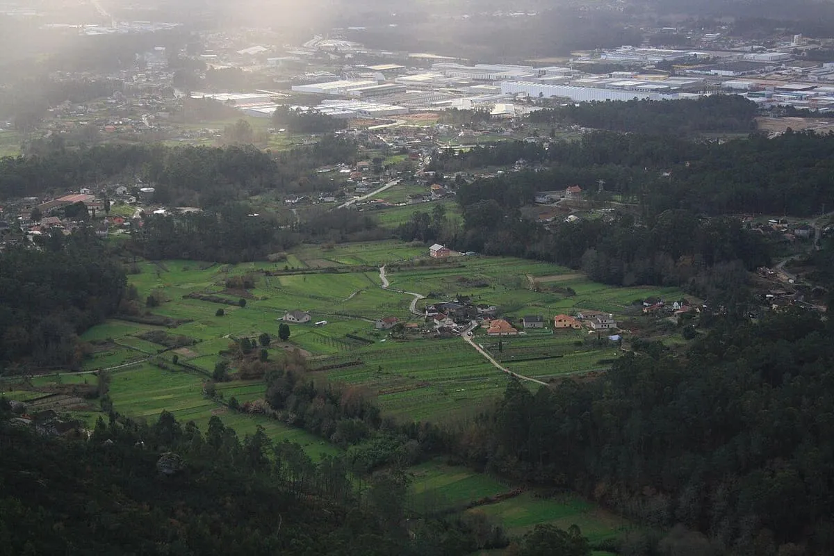 Vista desde lo alto sobre el valle de la Louriña, con prados verdes, casas y el monte