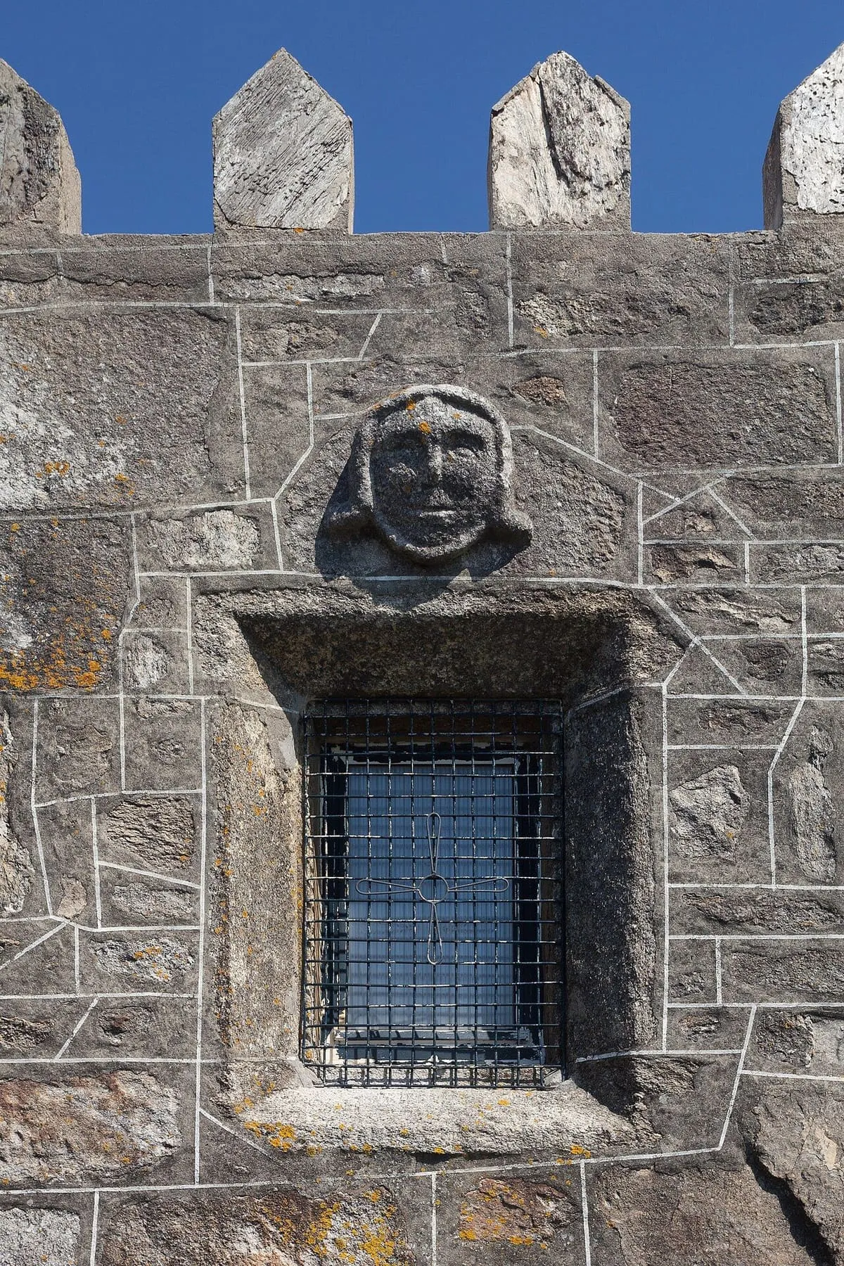 Rostro esculpido sobre la ventana enrejada de la capela da Atalaia, en un muro de sillares con grafitis antiguos